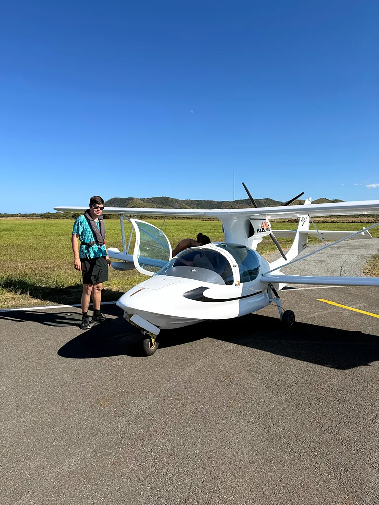 A white light amphibian aircraft on a small airfield apron, a man in a life vest beside it