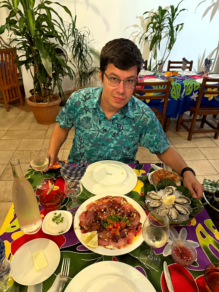 A man in glasses at a table with oysters, carpaccio and other dishes