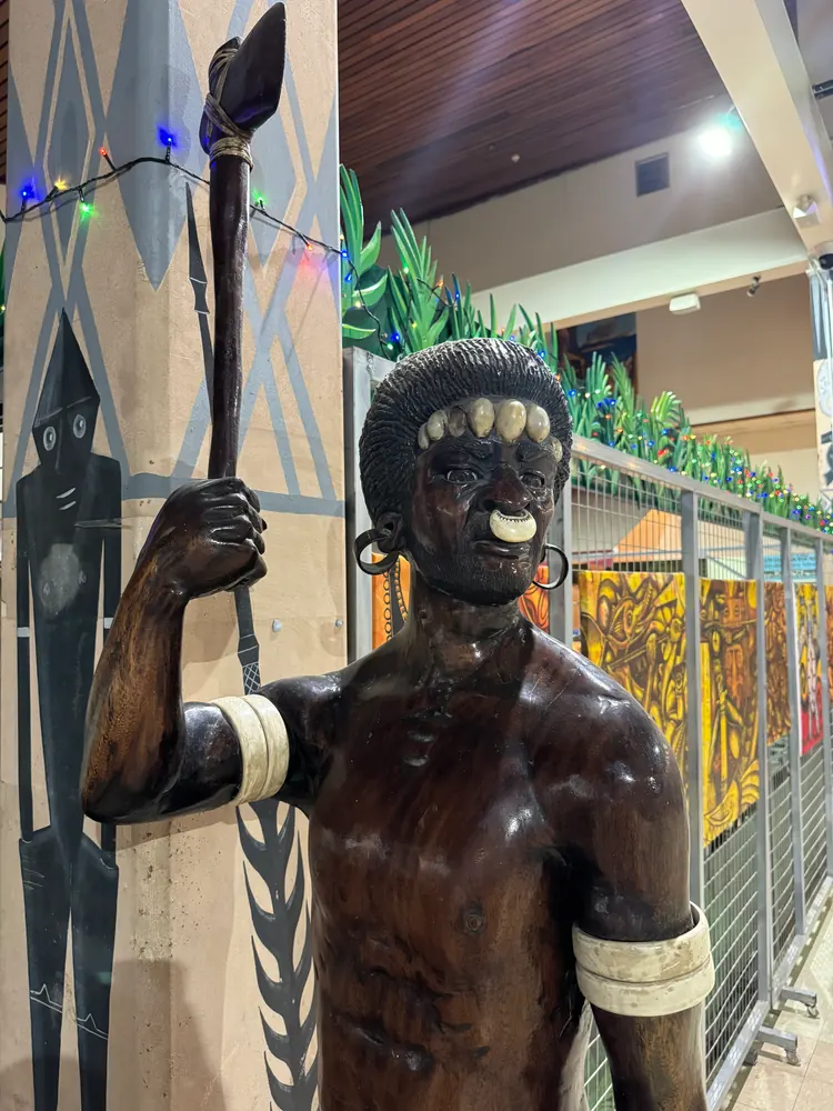 A carved wooden figure of a warrior with a torch, inside an airport