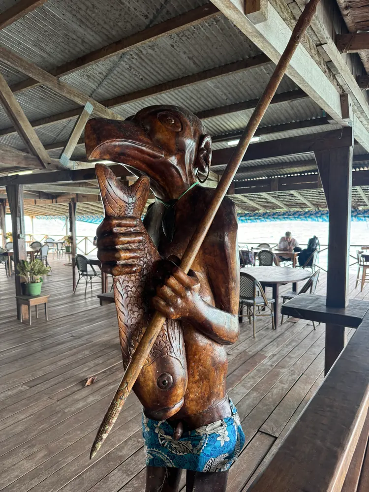 A carved wooden figure with a spear on a veranda by the water