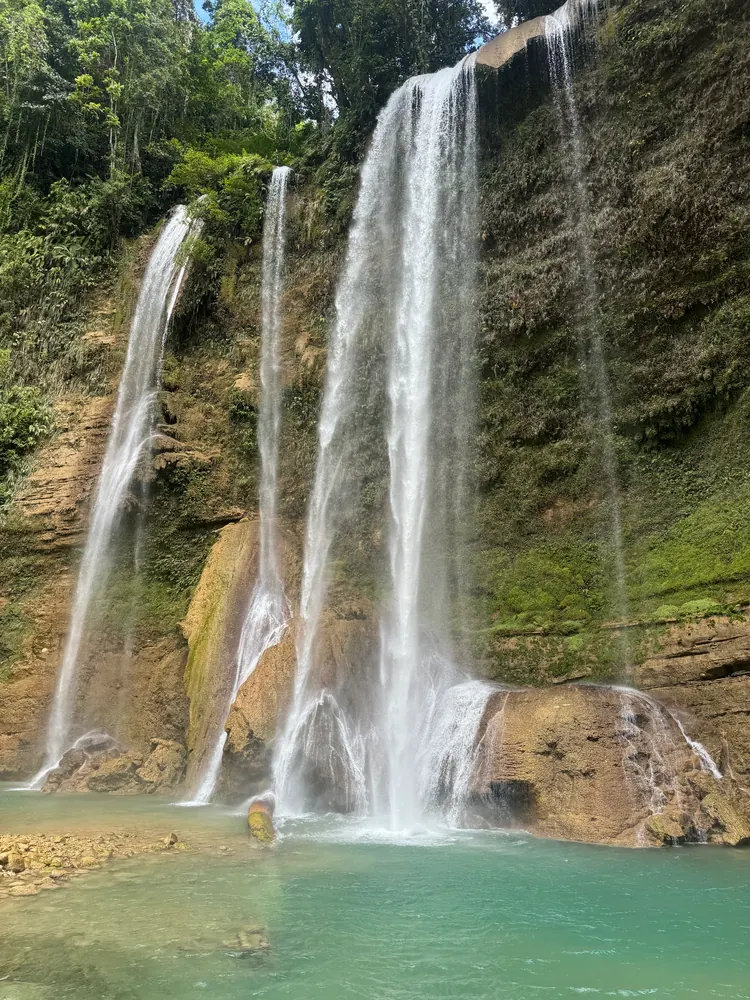 A waterfall in several streams falling from a rock ledge into a turquoise pool