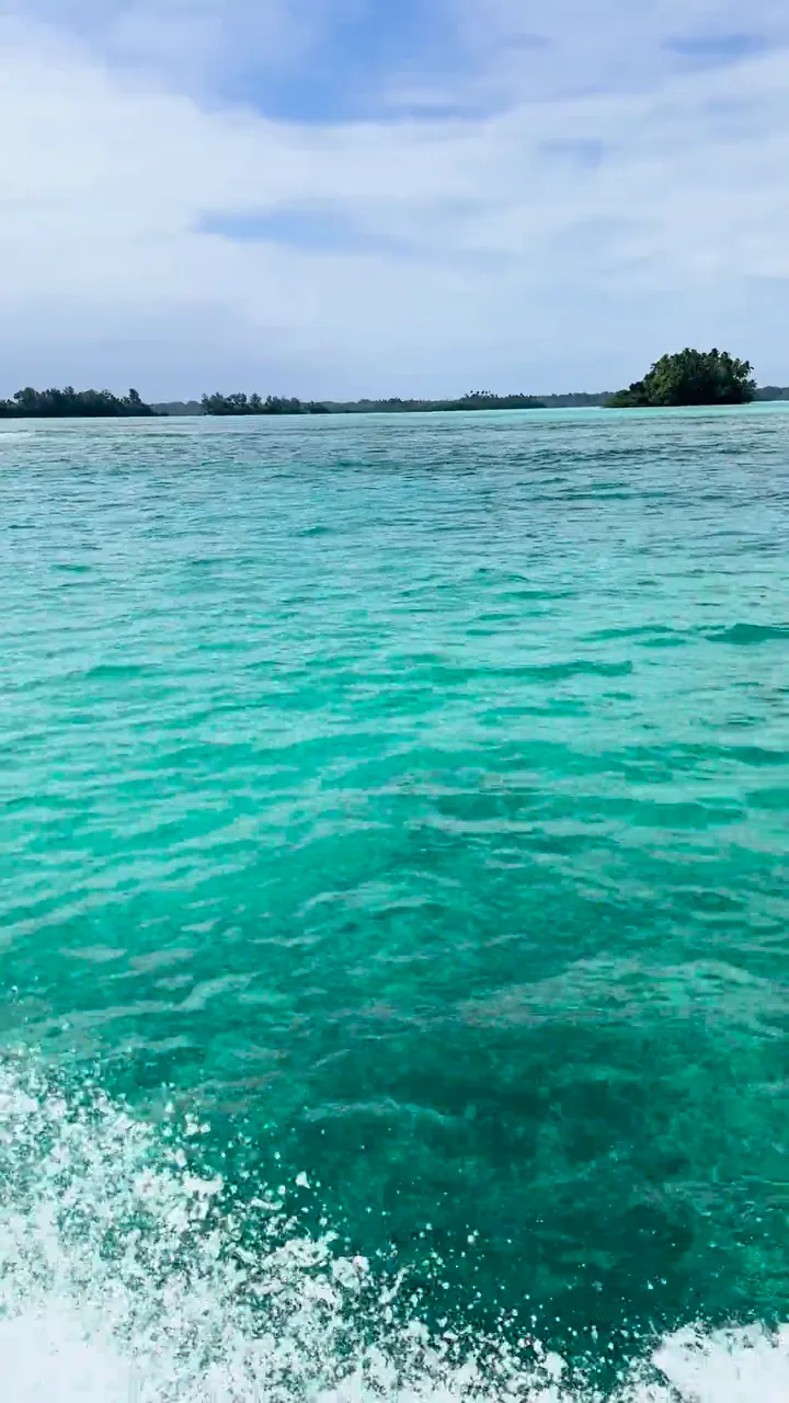 A boat moving through a shallow turquoise lagoon, with spray at the side