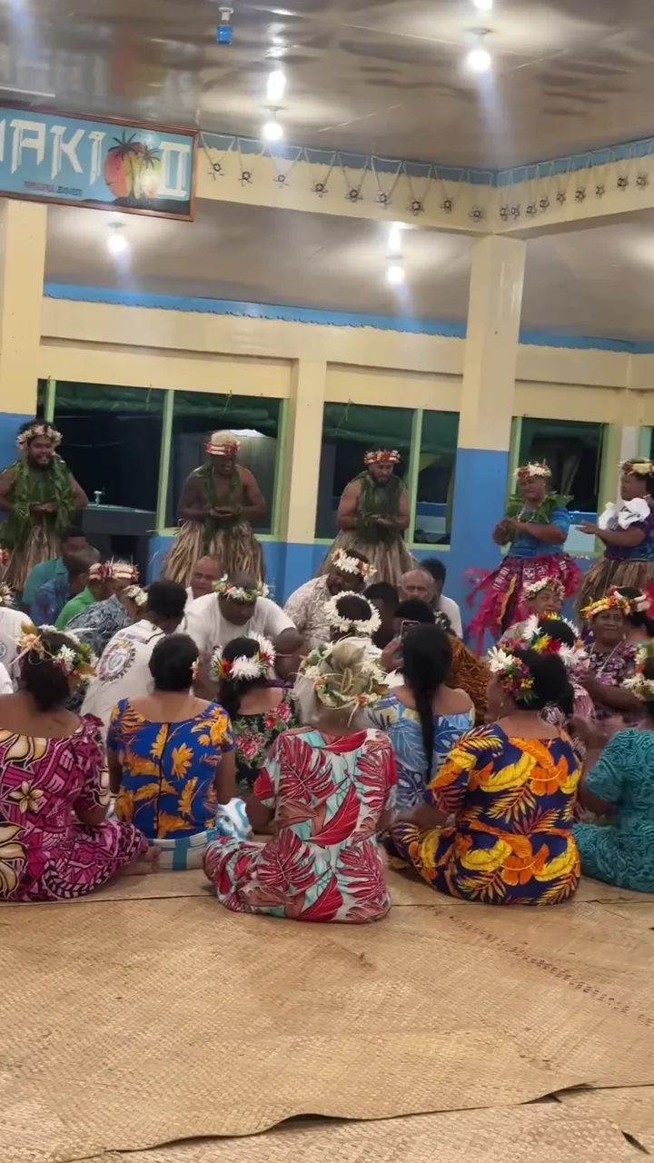 In a hall on Funafuti, people of different generations, including children, sing and dance to drums, clapping and a chorus.